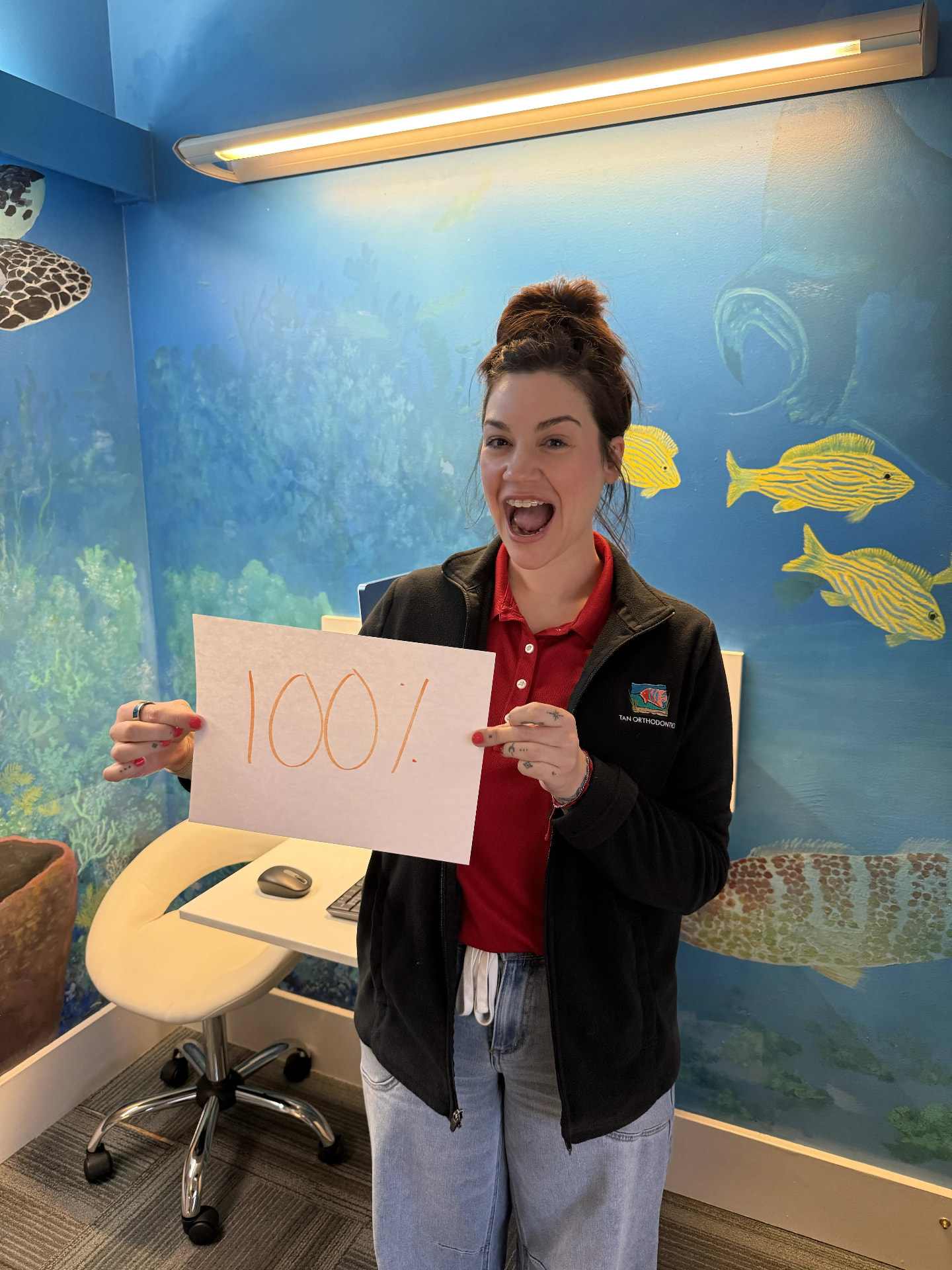 Tan Orthodontics team member holding a 100% sign in the under-the-sea consult room