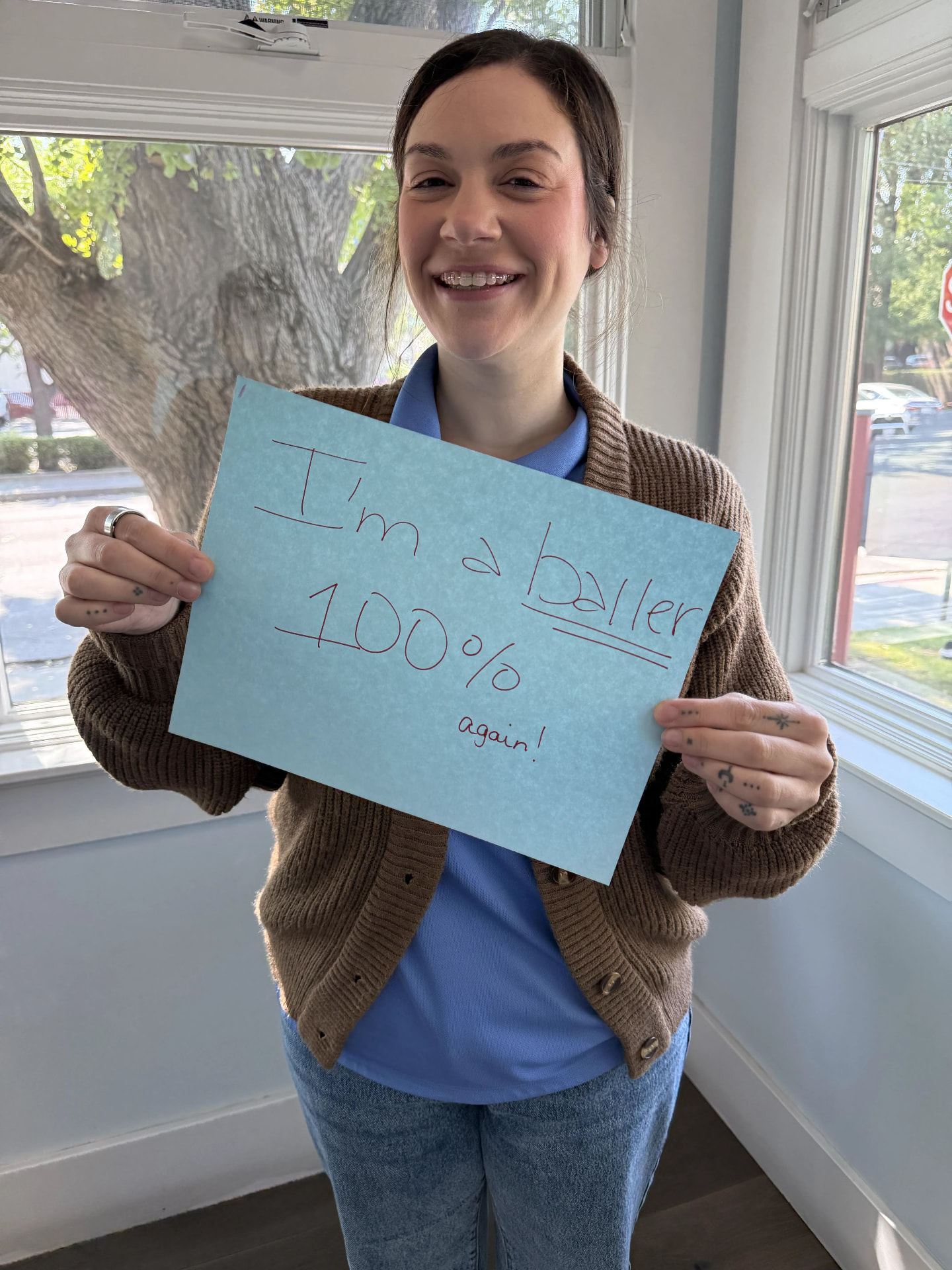 Tan Orthodontics team member holding an “I'm a baller — 100% again!” sign